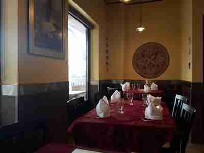 Cozy dine-in seating at Zeera By The Bay, featuring red tablecloths, folded white napkins, and wall art in a warm-lit atmosphere