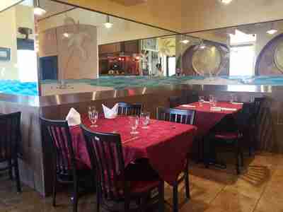 Elegant restaurant dining tables at Zeera By The Bay, with red covers, black chairs, and decorative mirrored wall featuring palm tree artwork