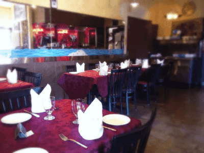 Indoor dining area at Zeera By The Bay set with white napkins, glassware, and polished red tablecloths in a modern restaurant interior